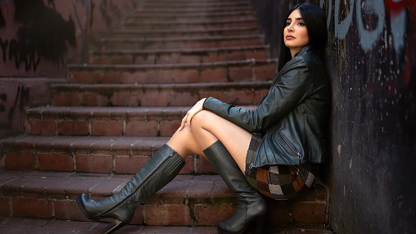 Момиче модел седи на стълби, облечено в черно кожено яке и ботуши на висок ток на фона на стената за рисуване Момичета HD тапет