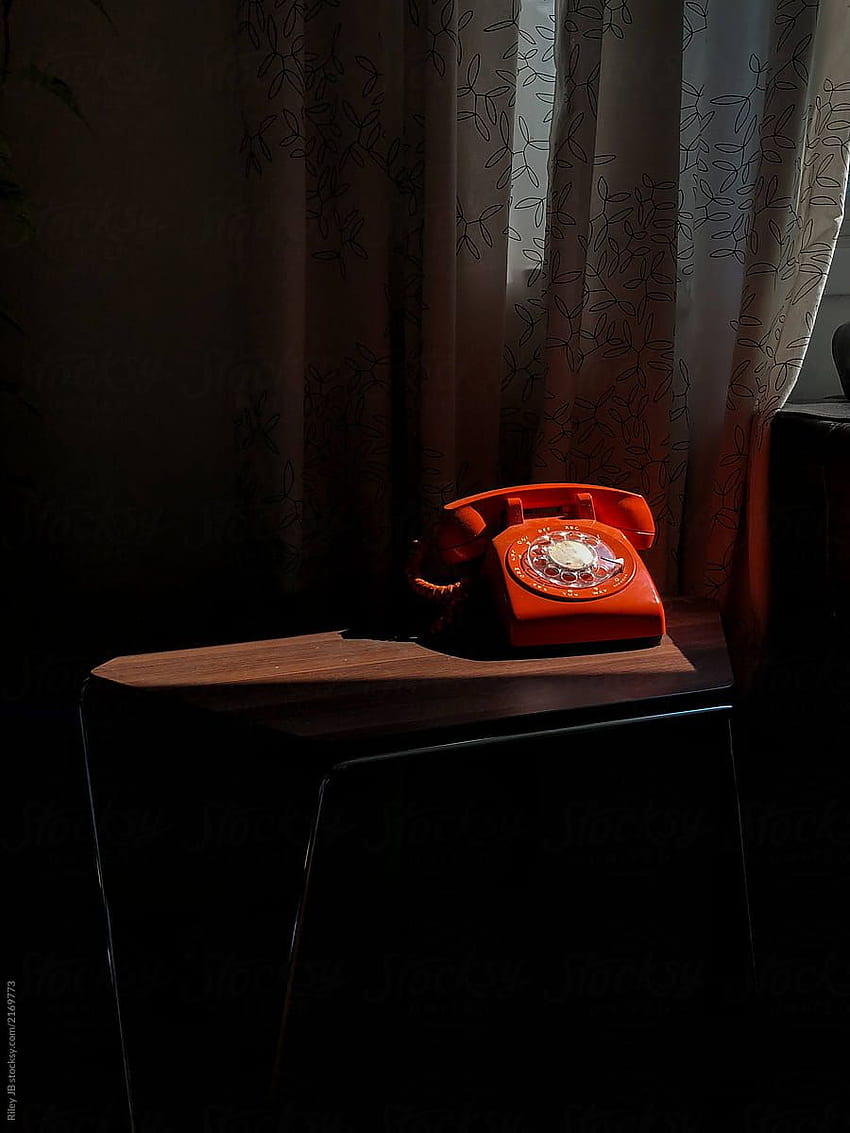 Altes orangefarbenes Telefon mit Wählscheibe in einem Sonnenstrahl an HD-Handy-Hintergrundbild