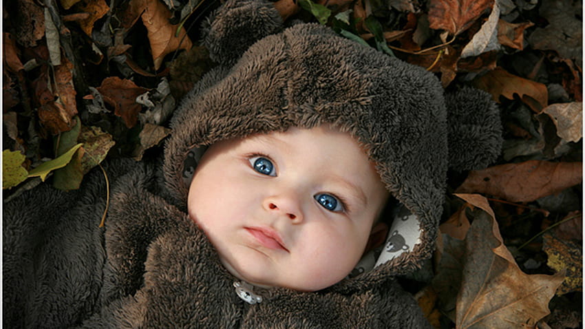 Blue Eyes Cute Baby Boy è sdraiato su foglie secche indossando un panno di pelliccia marrone Carino Sfondo HD