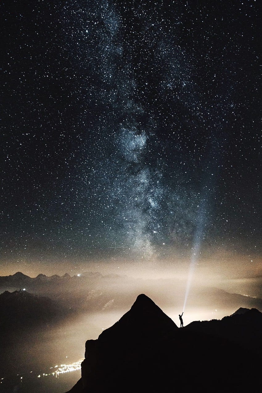silueta de persona en la cima de la montaña apuntando con una linterna en el cielo lleno de estrellas por la noche. Oscuro , Galaxia , Iphone negro oscuro fondo de pantalla del teléfono