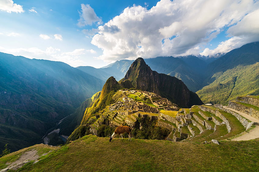 Machu Picchu illuminated by the warm sunset light. Wide angle view from the terraces above with scenic sky and sun burst. Dreamlike travel destination, world wonder. Cusco Region, Peru HD wallpaper