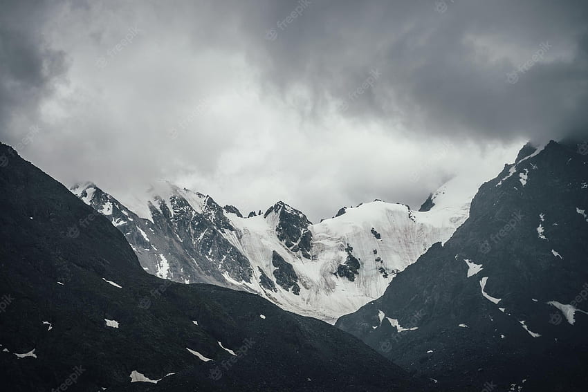 Premium . Ciemny atmosferyczny kraj górski z lodowcem na czarnych skałach w ołowianym szarym pochmurnym niebie. zaśnieżone góry w szarych niskich chmurach w deszczową pogodę. ponury kraj górski z górami skalistymi Tapeta HD