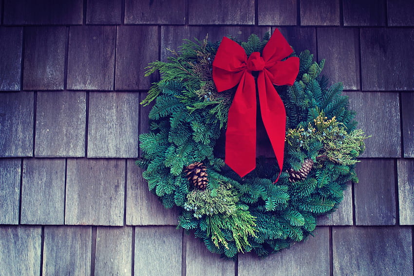 a christmas wreath with a red bow and pinecones hanging on the side HD wallpaper