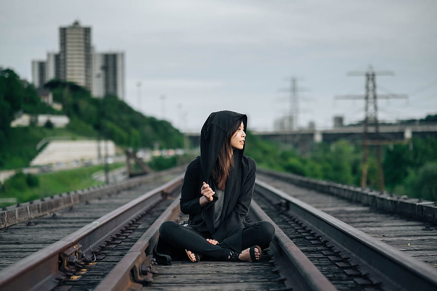 Mise au point sélective de la femme en sweat à capuche noir et pantalon assis sur la voie ferrée Fond d'écran HD
