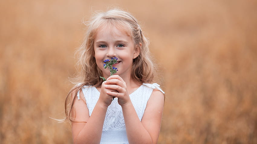 Усмихнато сладко момиченце със сини цветя стои на размазан фон, облечено в бяла рокля, сладко HD тапет