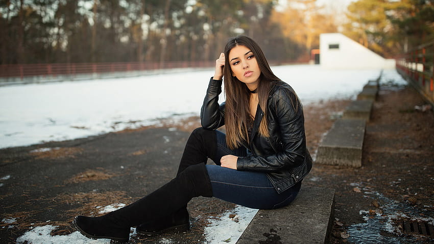 ブルネットの少女モデルは雪の中で座っている黒い革のジャケットを着ています ぼかしの背景の女の子 高画質の壁紙