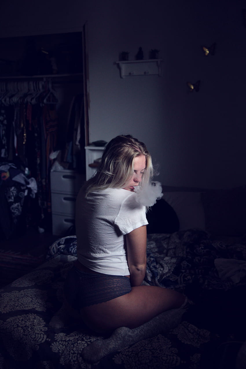 Donna che indossa una camicia bianca seduta sul divano e fuma · Stock Sfondo del telefono HD