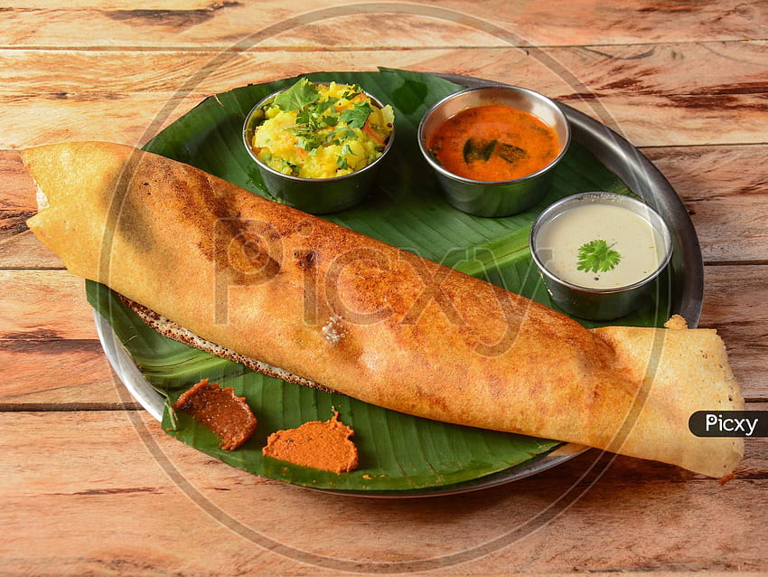 di Masala Dosa, una crêpe tradizionale e popolare dell'India meridionale con ripieno di una miscela di purè di patate e cipolle fritte servite con chutney e sambar su uno di legno rustico Sfondo HD