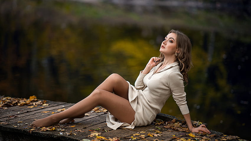 Linda modelo está sentada na doca de madeira em fundo desfocado usando vestido meio branco meninas papel de parede HD