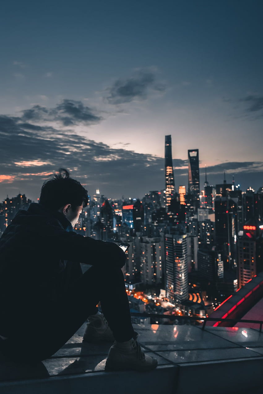 Mann sitzt nachts auf dem Dach – Mensch auf Unsplash. Stadtästhetik, futuristische Stadt, Stadtlandschaft, Dach bei Nacht HD-Handy-Hintergrundbild