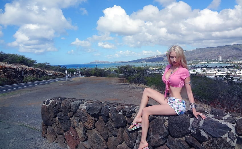 Valeria Lukyanova, road signs, blondde, hot pink blouse, blue pattern, jewelry, ocen in background, slipon heels, off the highway, white shorts with, sitting on stone wall HD wallpaper