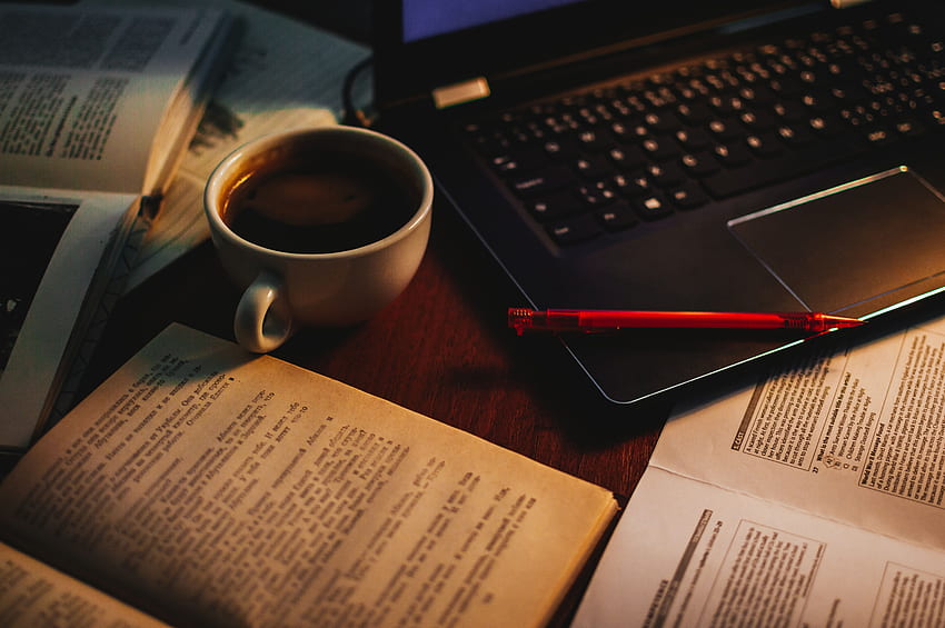 Tasse Kaffee zwischen offenem Buch und schwarzem Laptop HD-Hintergrundbild