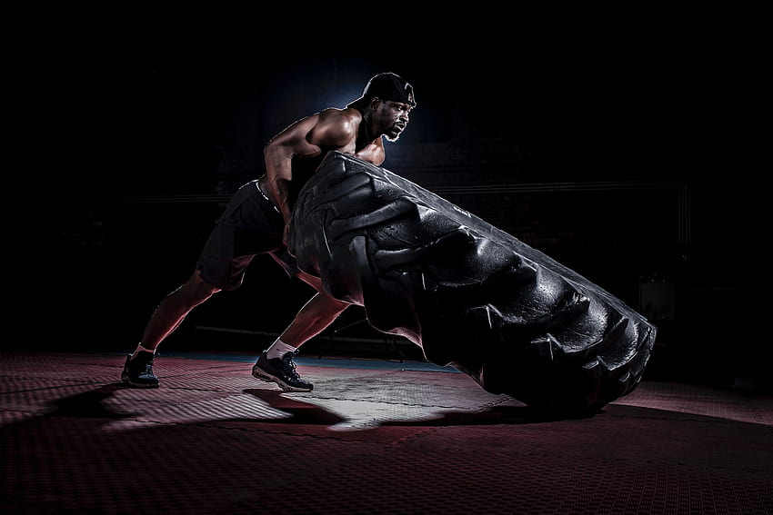 Strong shirtless black man flipping heavy tire in dark gym · Stock HD wallpaper