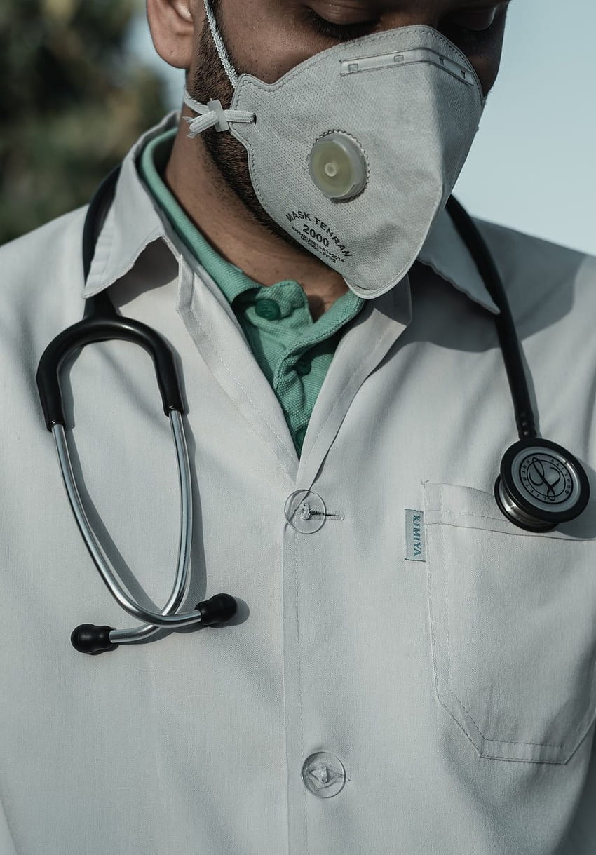 Horizontal view of smiling professional doctor works in clinic, poses at  modern hospital office with electronic gadgets, sends text messages on  cellphone being at work. Health care, technology concept - a Royalty