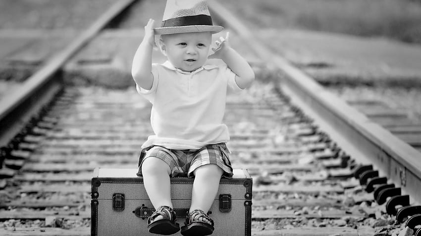 Czarno-biały ładny chłopczyk siedzi na pudełko podróżne w torach kolejowych rozmycie tła słodkie Tapeta HD