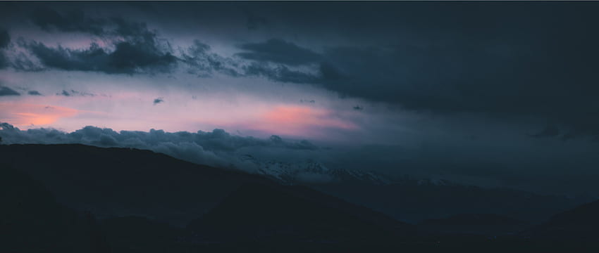 / Nubes oscuras ruedan sobre las siluetas de las colinas al atardecer, paisaje nublado por la noche fondo de pantalla