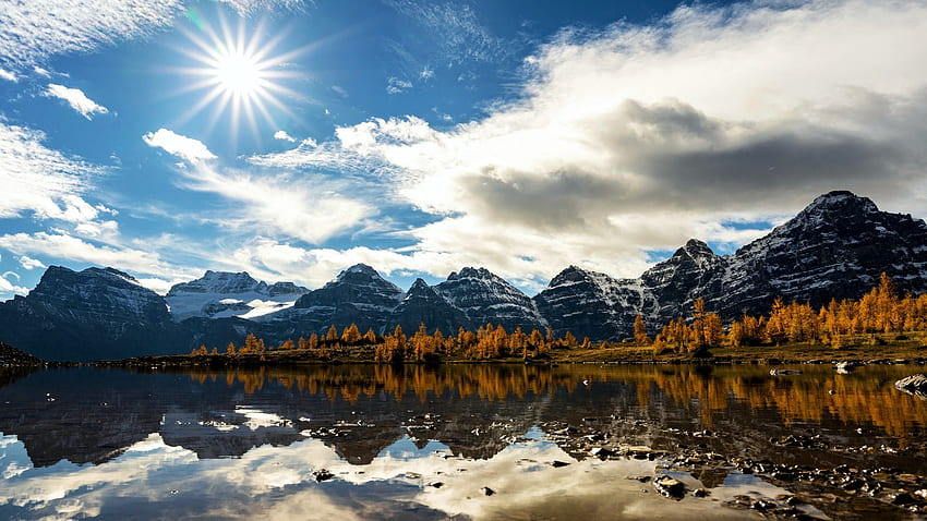 Златни лиственици край езерото Морейн, Албърта, планини, Канада, слънце, есен, цветове, пейзаж, камъни, отражения, дървета, облаци, небе, вода HD тапет