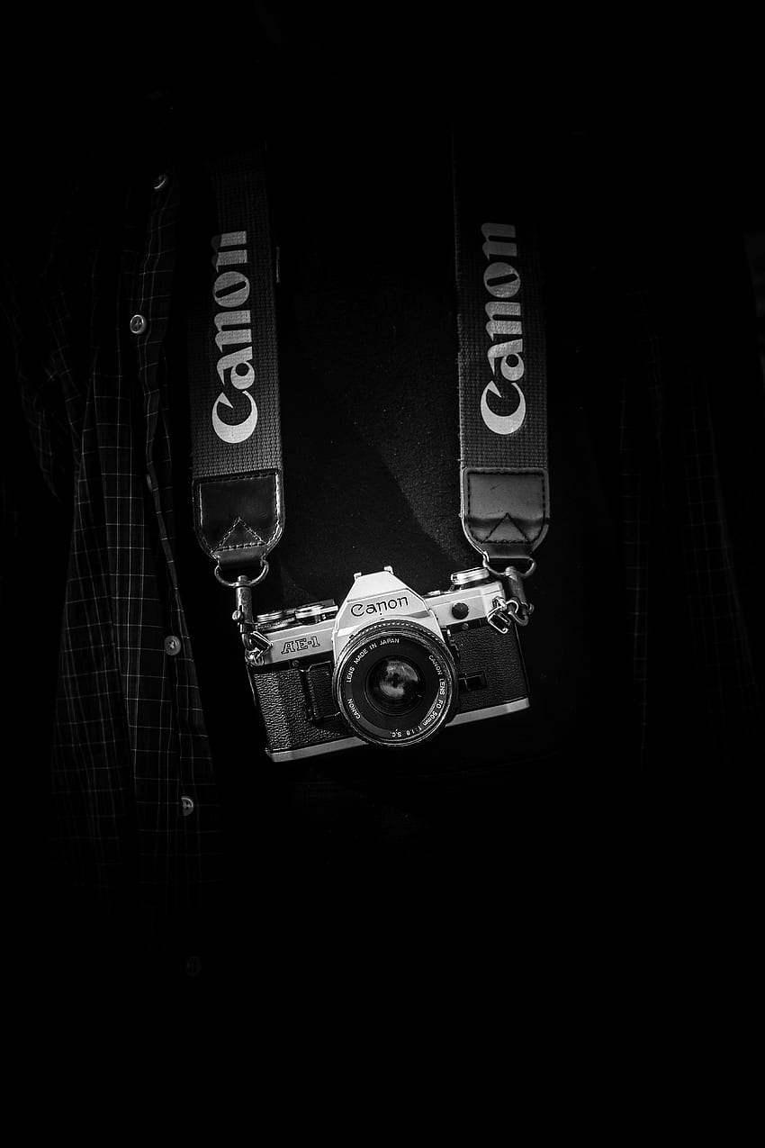 / toma en blanco y negro de una cámara canon con una correa en el torso con camisa a cuadros, la cámara canon monocromática cuelga fondo de pantalla del teléfono