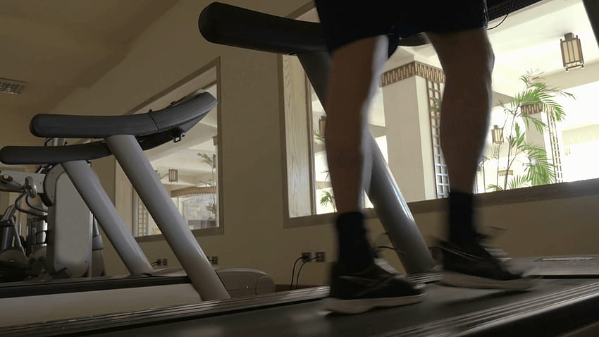 Tiefwinkelaufnahme eines Mannes, der auf dem Laufband trainiert, wobei nur die Füße zu sehen sind. Fitnessraum im Hotel mit Hallenblick Stock Video Footage HD-Hintergrundbild