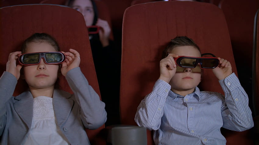 Children wearing 3D glasses at cinema chair. Brother and sister watching 3D film together in slow motion. Boy and girl watching 3D cartoon at movie theater. Modern movie entertainment for kids Stock HD wallpaper