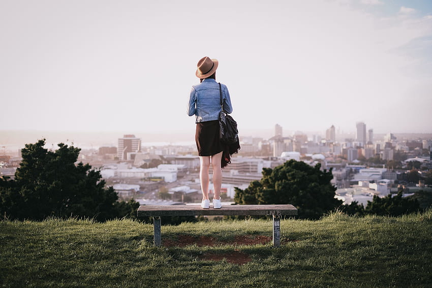 / mulher em pé em um banco de parque e examinando a cidade abaixo, o horizonte papel de parede HD