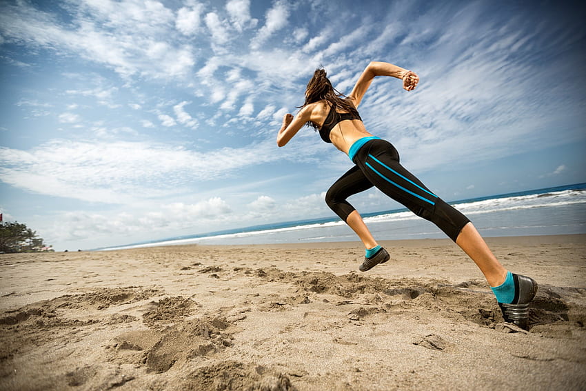 Frau in schwarzem Sport-BH und Trainingshose, die am Strand läuft HD-Hintergrundbild
