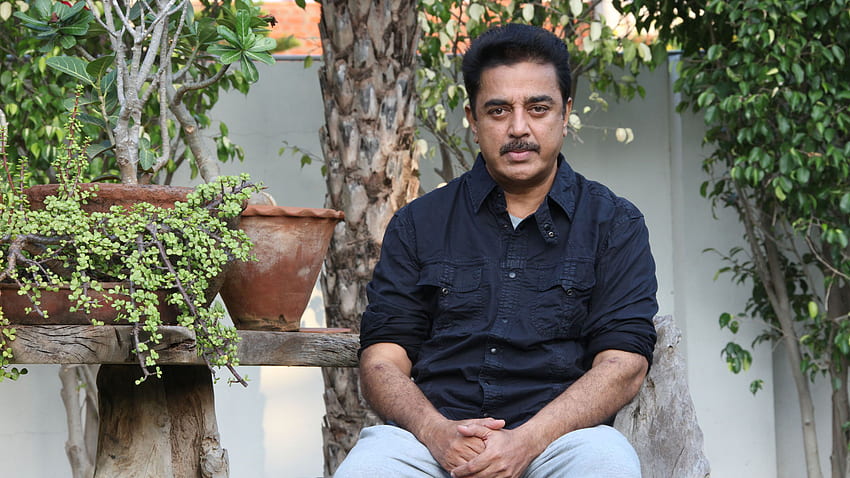 Schauspieler Kamal Hassan trägt ein schwarzes Hemd und eine weiße Hose, die im Hintergrund der grünen Pflanzen sitzt HD-Hintergrundbild