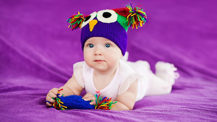 Cute Girl Baby è sdraiato su un morbido panno viola che indossa un abito bianco e un berretto a maglia di lana colorato Carino Sfondo HD