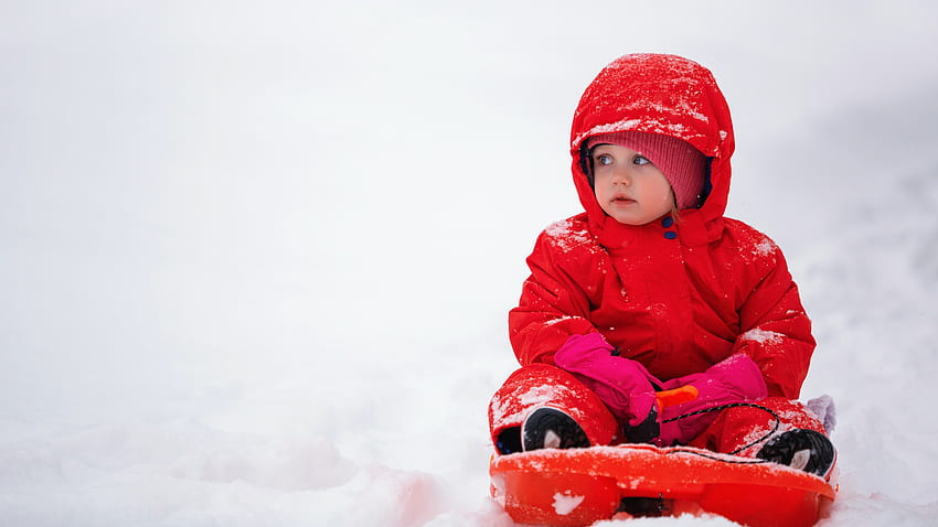 Niño pequeño lindo está sentado en la nieve en blanco con vestido de punto de lana roja y gorro lindo fondo de pantalla