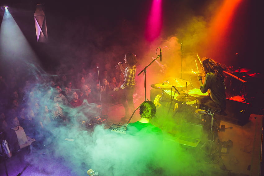 / una band che si esibisce sul palco con luci color arcobaleno che li inondano dall'alto, band in fumo arcobaleno Sfondo HD