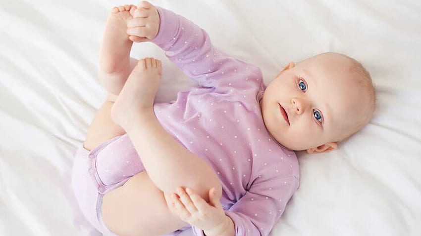 Simpatico bambino carino è sdraiato su un panno bianco che indossa un abito viola chiaro carino Sfondo HD